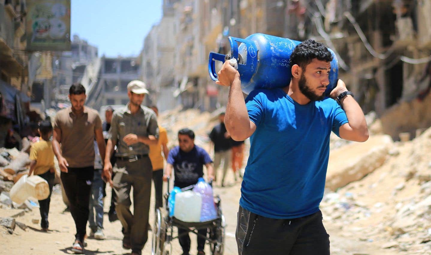Un Palestinien transporte un réservoir de gaz à travers les ruines de Khan Younès, mercredi.